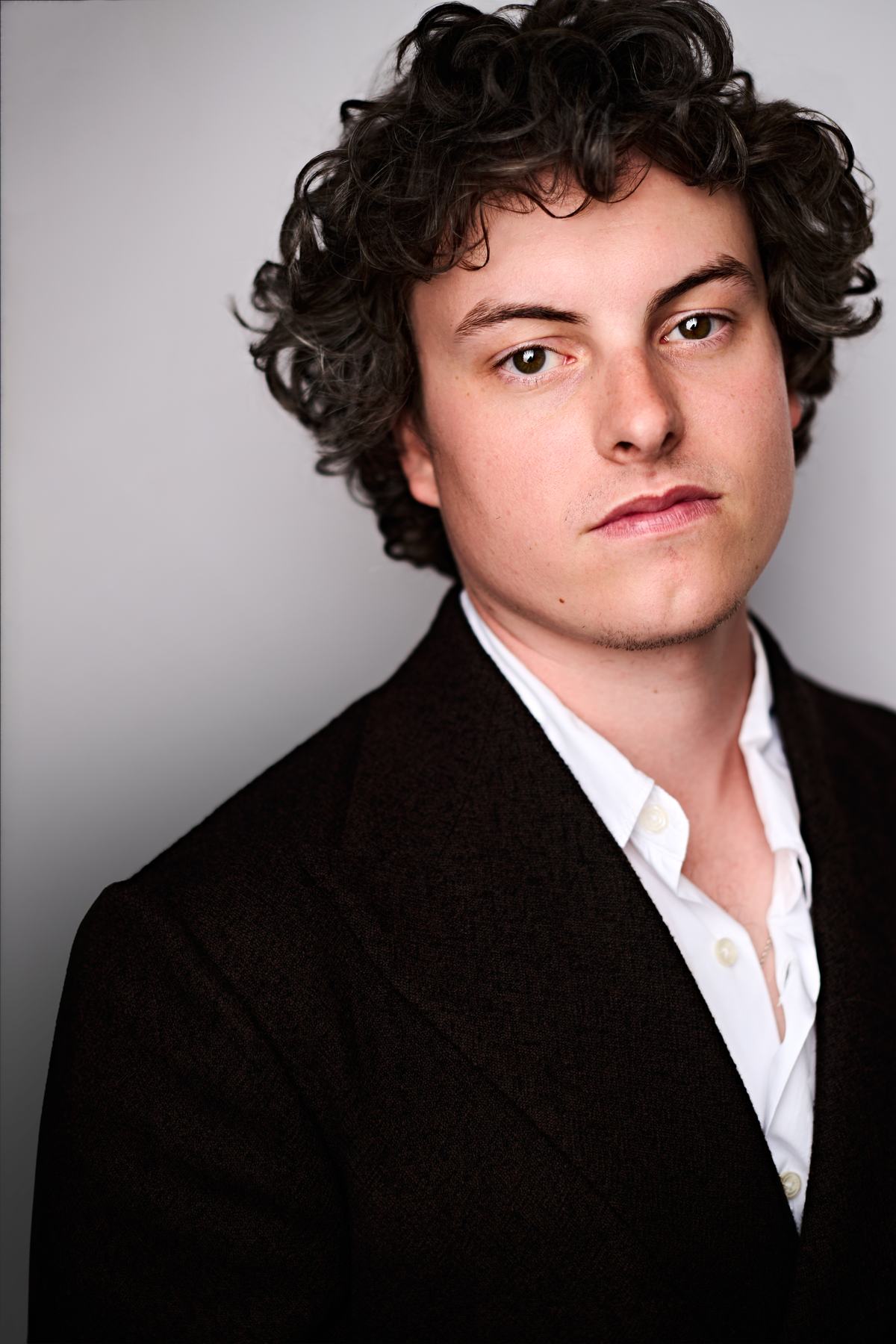 Frankie Seratch, dark blazer over an open white shirt against a grey ground